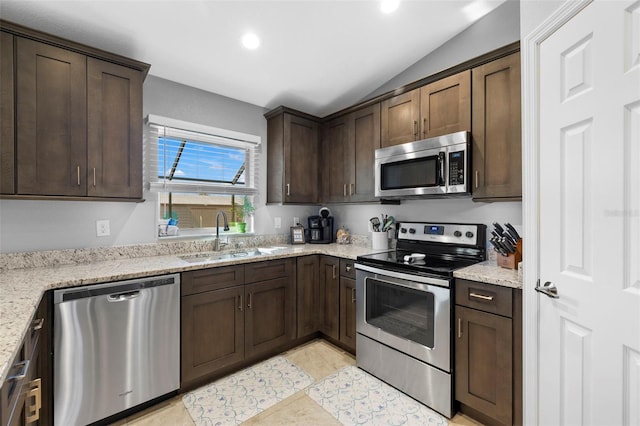 kitchen featuring sink, vaulted ceiling, light stone countertops, dark brown cabinetry, and stainless steel appliances