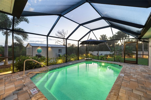 pool at dusk featuring glass enclosure, a patio area, and an outdoor structure