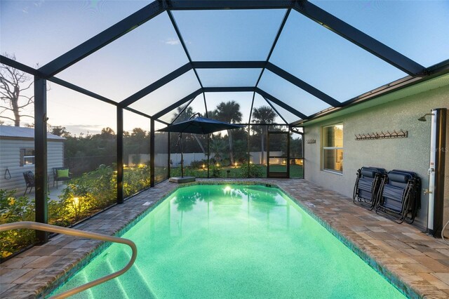 pool at dusk with a patio and glass enclosure