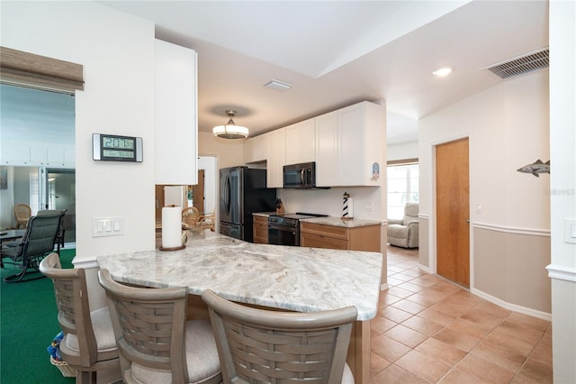 kitchen with black appliances, light stone counters, white cabinetry, a breakfast bar, and kitchen peninsula