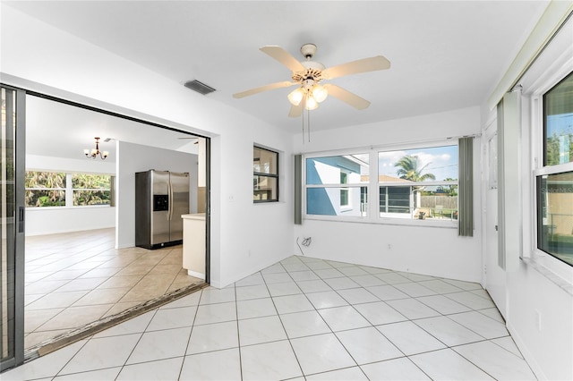 tiled empty room with ceiling fan with notable chandelier