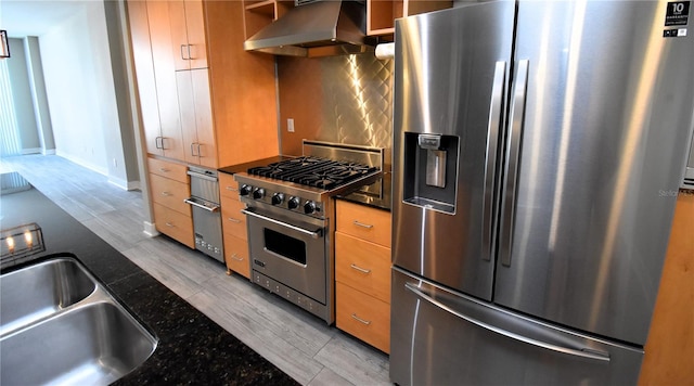 kitchen with light wood-type flooring, stainless steel appliances, sink, dark stone countertops, and range hood