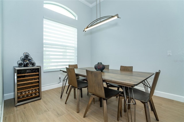 dining space with ornamental molding, beverage cooler, and light wood-type flooring