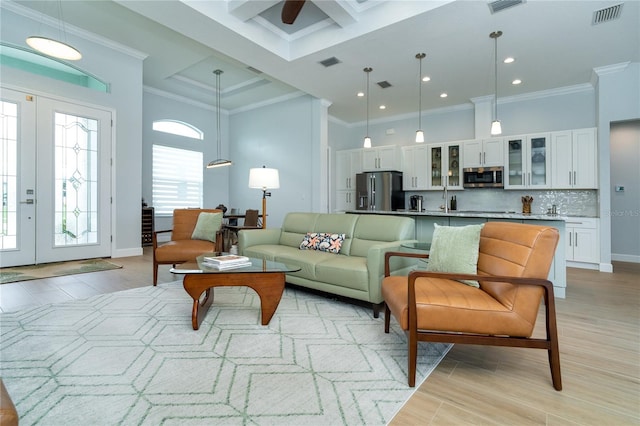 living room featuring sink, a high ceiling, ornamental molding, french doors, and light wood-type flooring