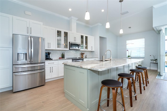 kitchen with appliances with stainless steel finishes, a kitchen island with sink, hanging light fixtures, light stone counters, and white cabinets