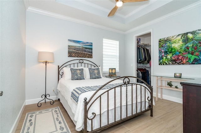 bedroom with a spacious closet, ornamental molding, a tray ceiling, a closet, and hardwood / wood-style floors