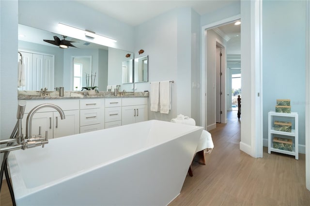 bathroom with wood-type flooring, vanity, ceiling fan, crown molding, and a bath