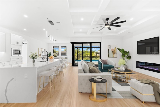 living room featuring beamed ceiling, light wood-type flooring, ceiling fan, and coffered ceiling