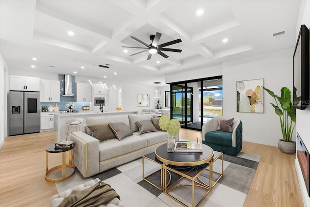 living room featuring ceiling fan, light hardwood / wood-style flooring, beamed ceiling, and coffered ceiling