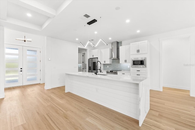 kitchen with a large island, wall chimney exhaust hood, light hardwood / wood-style flooring, decorative light fixtures, and appliances with stainless steel finishes