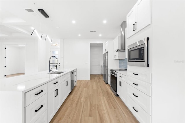 kitchen with sink, wall chimney exhaust hood, stainless steel appliances, white cabinets, and light wood-type flooring