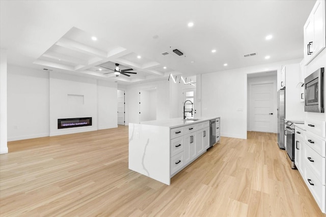 kitchen featuring white cabinets, sink, light wood-type flooring, an island with sink, and appliances with stainless steel finishes