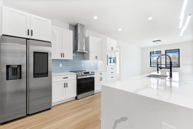 kitchen featuring light hardwood / wood-style flooring, white cabinets, stainless steel appliances, and wall chimney range hood