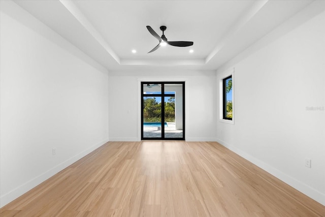 empty room featuring ceiling fan, light hardwood / wood-style floors, and a tray ceiling