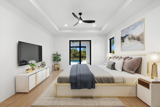 bedroom featuring ceiling fan, light wood-type flooring, and a tray ceiling