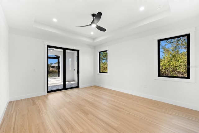 spare room featuring a tray ceiling, ceiling fan, light hardwood / wood-style flooring, and plenty of natural light