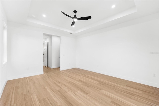 spare room with a tray ceiling, ceiling fan, and light hardwood / wood-style flooring