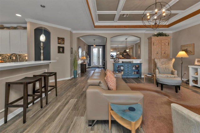 living room with coffered ceiling, sink, crown molding, wood-type flooring, and a chandelier