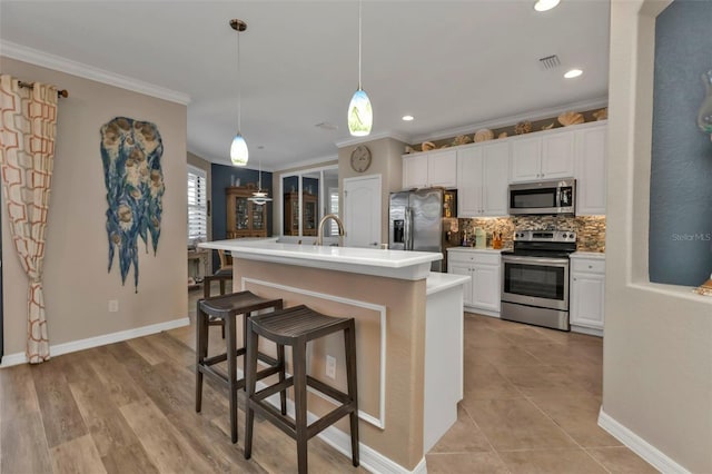 kitchen featuring white cabinetry, hanging light fixtures, backsplash, stainless steel appliances, and an island with sink