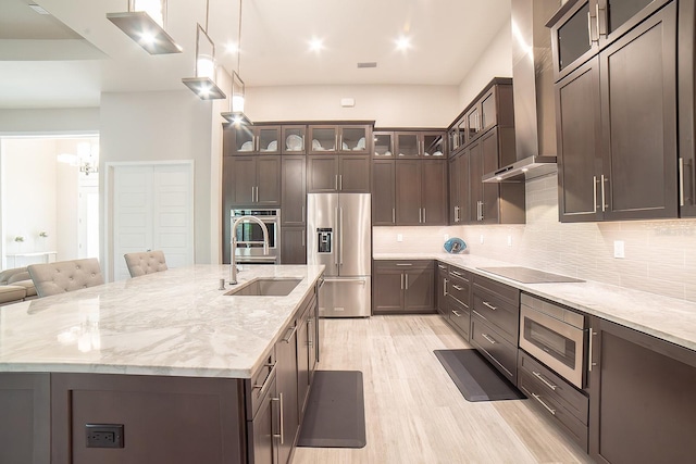 kitchen featuring sink, wall chimney exhaust hood, light stone counters, dark brown cabinets, and appliances with stainless steel finishes