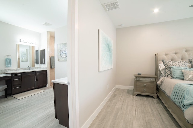 bedroom with light wood-type flooring, ensuite bath, and sink