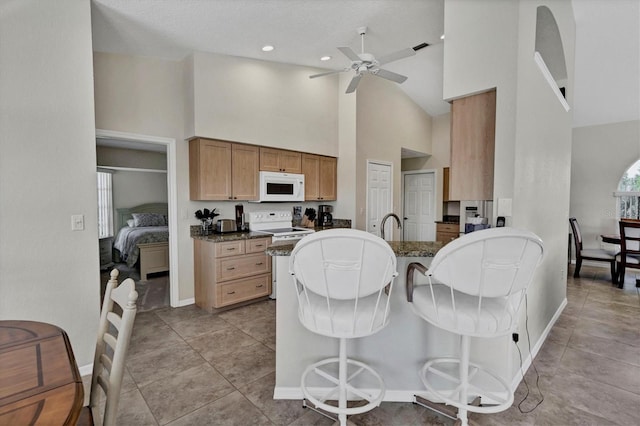 kitchen with a kitchen breakfast bar, dark stone counters, white appliances, ceiling fan, and high vaulted ceiling