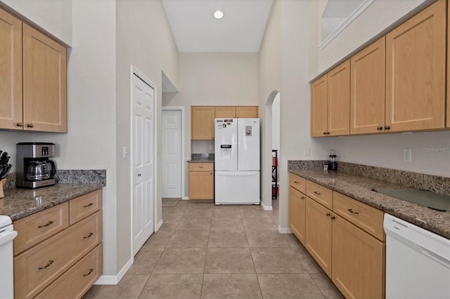 kitchen featuring light brown cabinets, light tile patterned floors, dark stone counters, and white appliances