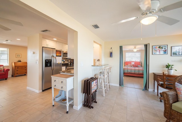 kitchen featuring white cabinetry, light stone countertops, stainless steel appliances, backsplash, and a breakfast bar area