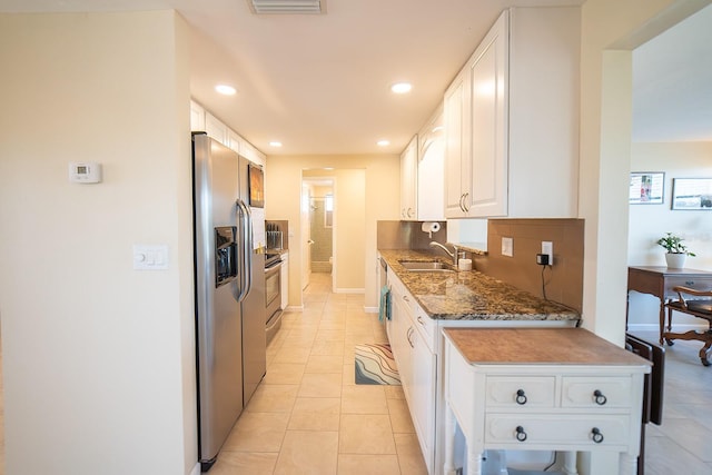 kitchen with stainless steel appliances, sink, light tile patterned floors, dark stone countertops, and white cabinetry