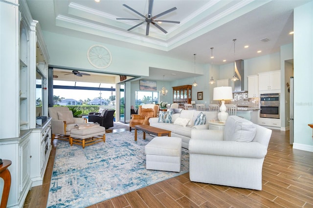 living room with a raised ceiling, crown molding, ceiling fan, and hardwood / wood-style flooring