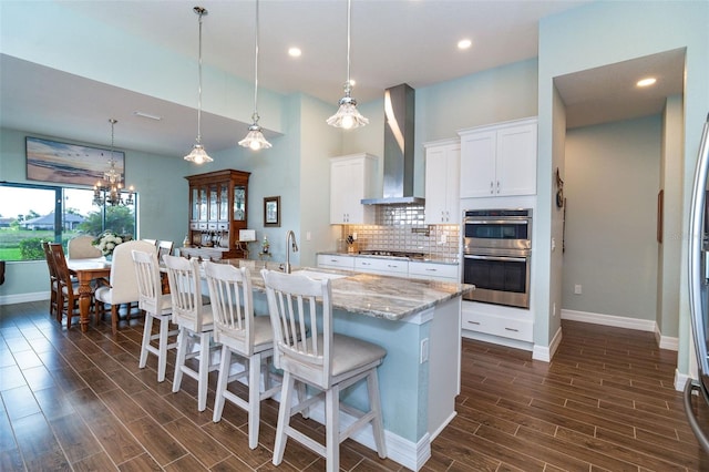 kitchen with appliances with stainless steel finishes, wall chimney exhaust hood, pendant lighting, white cabinetry, and a large island