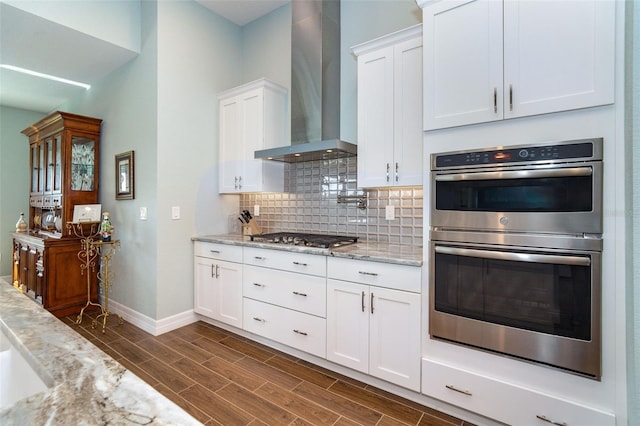 kitchen with white cabinetry, dark hardwood / wood-style flooring, wall chimney range hood, light stone countertops, and stainless steel appliances