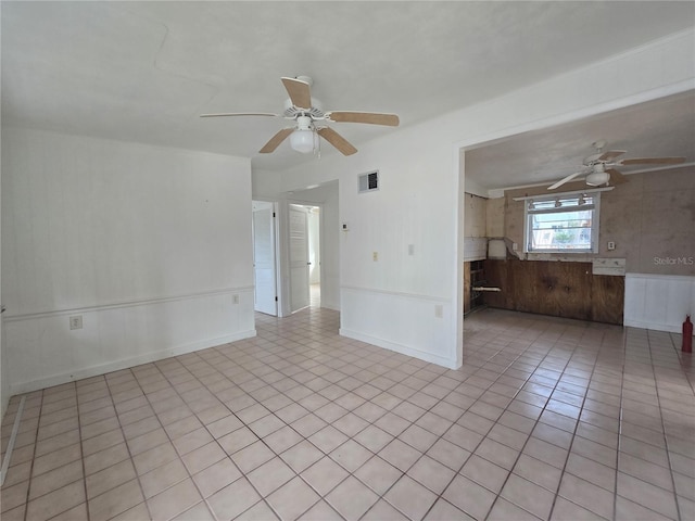 empty room with light tile patterned floors, ceiling fan, and wood walls