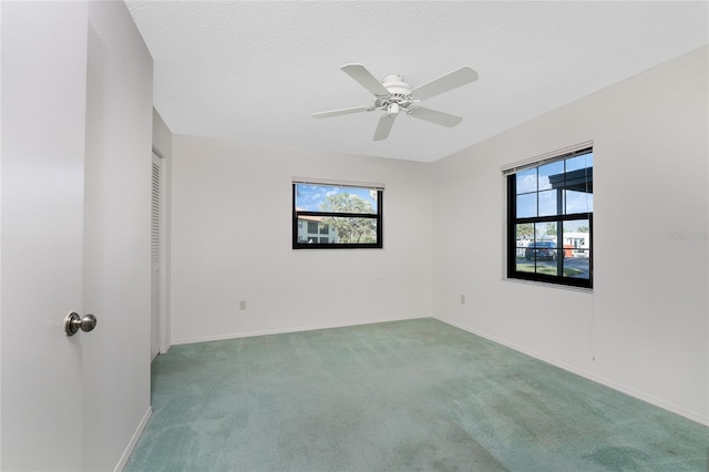 empty room with ceiling fan, plenty of natural light, carpet floors, and a textured ceiling