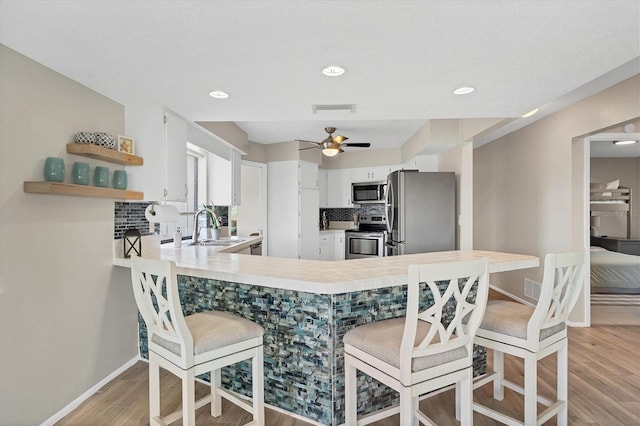 kitchen with white cabinetry, sink, stainless steel appliances, kitchen peninsula, and a kitchen bar