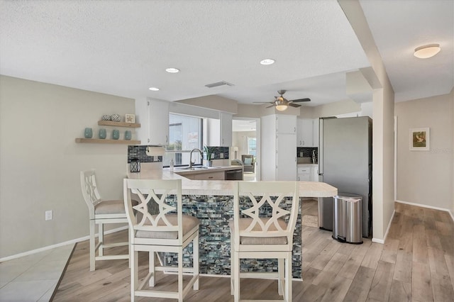 kitchen with kitchen peninsula, light wood-type flooring, white cabinetry, a breakfast bar area, and stainless steel appliances