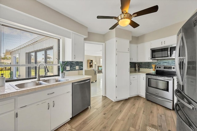 kitchen with appliances with stainless steel finishes, backsplash, sink, white cabinets, and light hardwood / wood-style floors