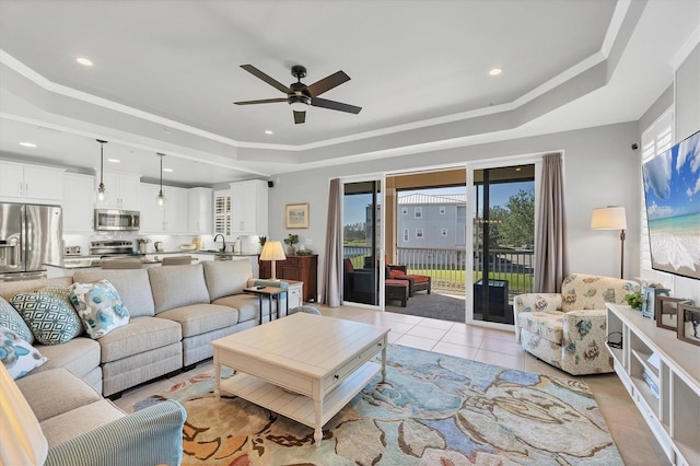 tiled living room with a raised ceiling, ceiling fan, and sink