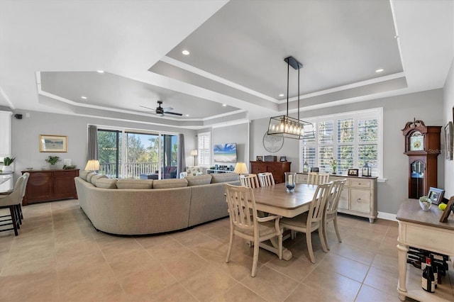 tiled dining space featuring ceiling fan with notable chandelier and a raised ceiling