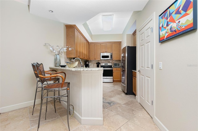 kitchen featuring a breakfast bar, appliances with stainless steel finishes, kitchen peninsula, and tasteful backsplash