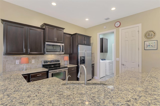 kitchen with dark brown cabinetry, light stone countertops, stainless steel appliances, separate washer and dryer, and backsplash