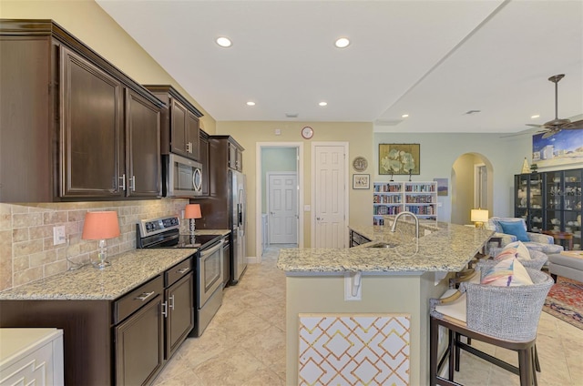 kitchen featuring light stone countertops, backsplash, stainless steel appliances, sink, and a breakfast bar area