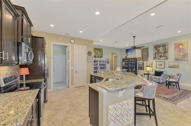 kitchen with backsplash, a center island with sink, sink, light stone counters, and stainless steel appliances