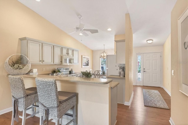 kitchen featuring dark wood-type flooring, a breakfast bar area, kitchen peninsula, pendant lighting, and white appliances