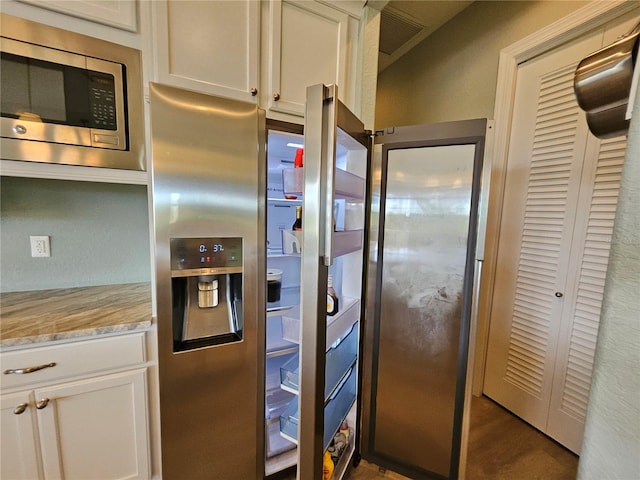 kitchen with white cabinetry, stainless steel microwave, and light stone countertops