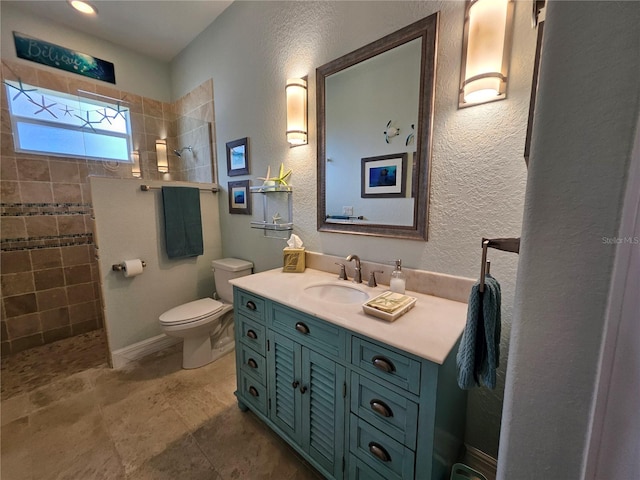 bathroom featuring toilet, a tile shower, and vanity