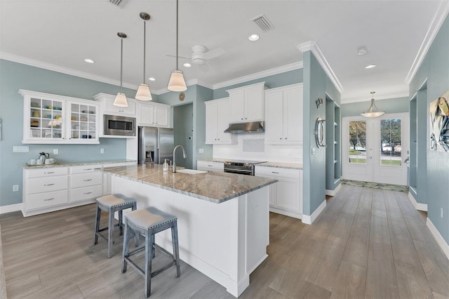 kitchen with appliances with stainless steel finishes, a kitchen island with sink, sink, decorative light fixtures, and light hardwood / wood-style floors