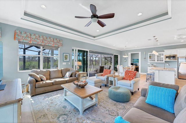 living room featuring a tray ceiling, ornamental molding, sink, and light hardwood / wood-style flooring