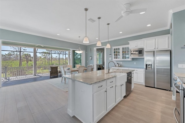 kitchen with appliances with stainless steel finishes, a center island with sink, light stone counters, decorative light fixtures, and white cabinetry