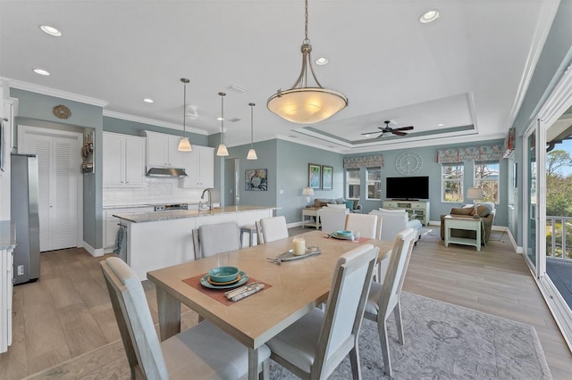 dining room with light hardwood / wood-style flooring, sink, ornamental molding, ceiling fan, and a raised ceiling